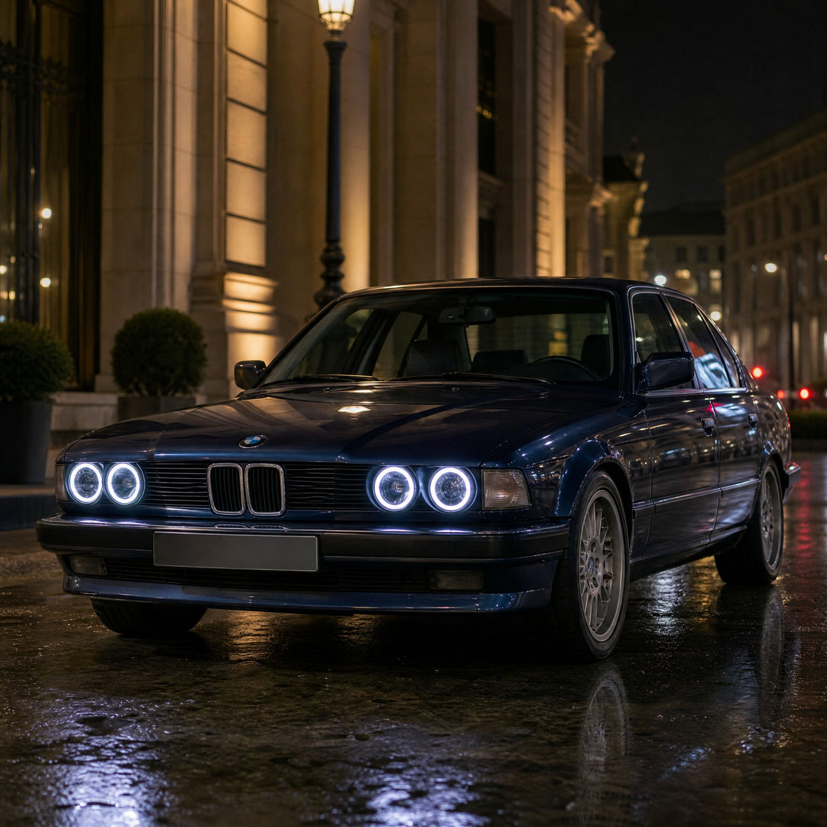 BMW Serie 7 E32 berlina blu scuro, di notte, con angel eyes LED bianchi intorno ai suoi quattro fari