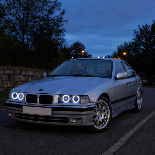 BMW Serie 3 E36 berlina gris plata al anochecer con aros LED blancos de ojos de ángel, dos por faro
