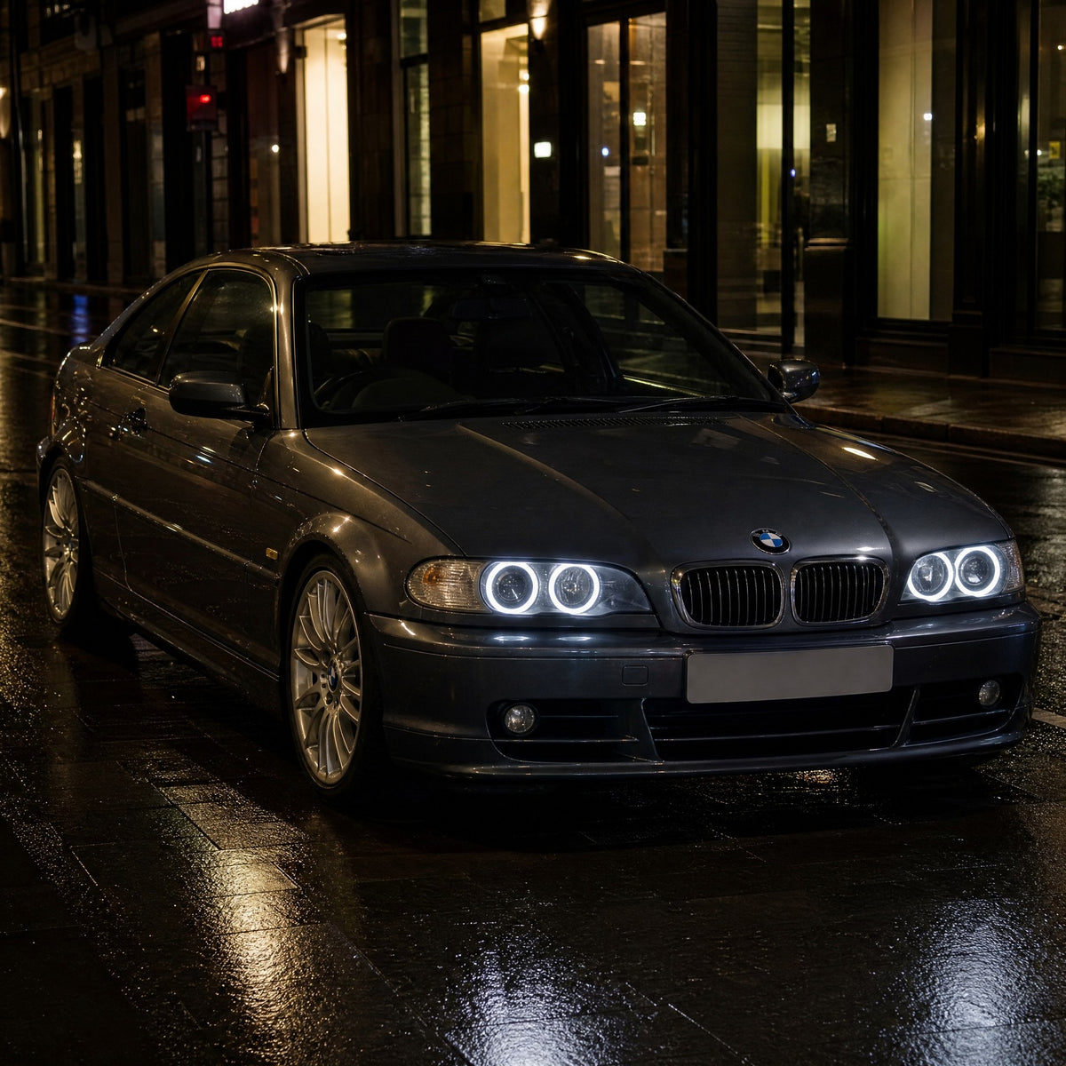 BMW Série 3 E46 coupé cinzento-escuro, à noite, numa rua molhada, com angel eyes LED brancos, dois anéis por farol