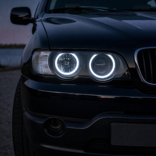 Grande plano do farol de um BMW X5 E53 preto anterior ao restyling, ao anoitecer, com dois anéis LED brancos de angel eyes acesos