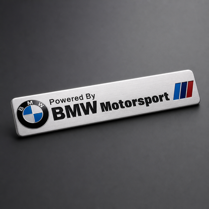 Emblema metálico adhesivo para tu BMW plata cepillado / logo BMW redondo + texto "Powered By BMW Motorsport" / 120 × 26 mm - packshot frontal con acabado deportivo